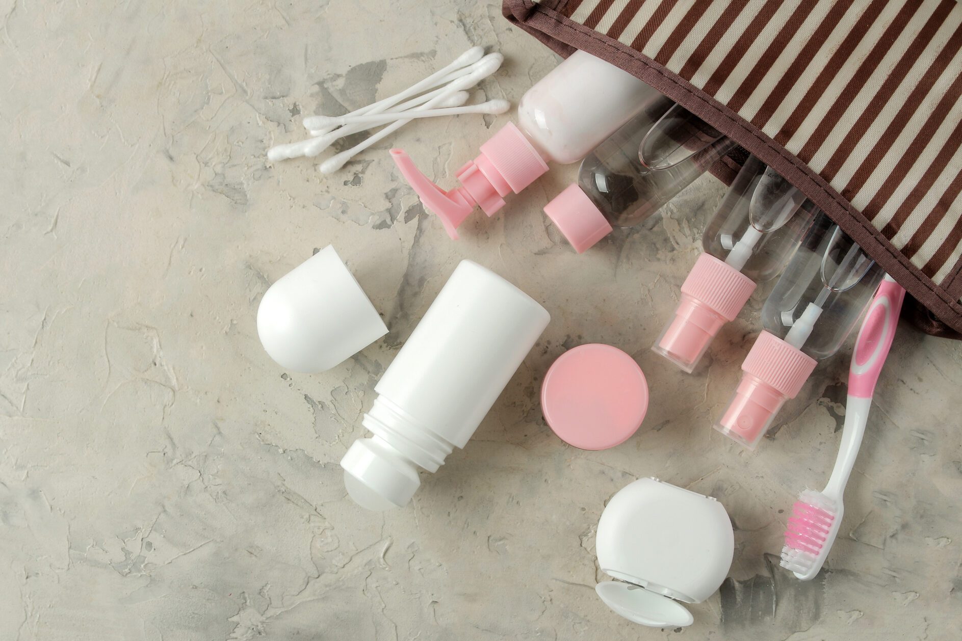 A set of cosmetics and personal care products for travel in a cosmetic bag on a light concrete background. top view. travel cosmetics