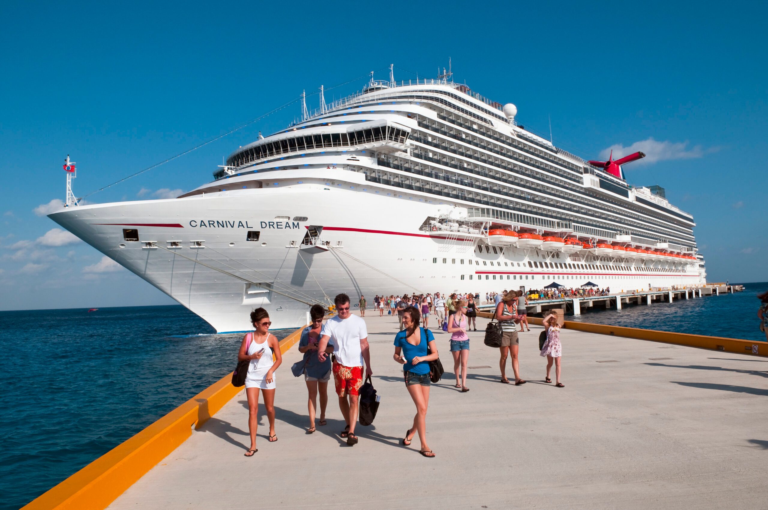 Carnival Cruise ship docked in blue water and sunny skies with passengers walking on the dock away from the ship