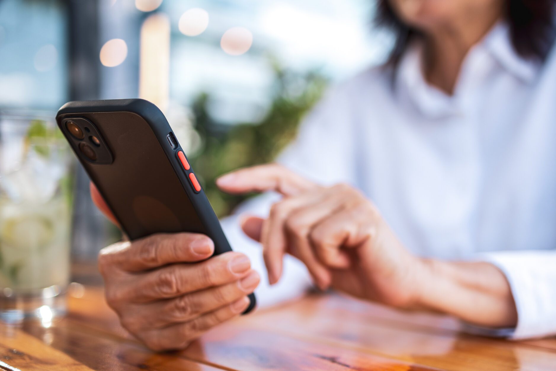 Focused user navigating smartphone while seated at a wooden table outdoors