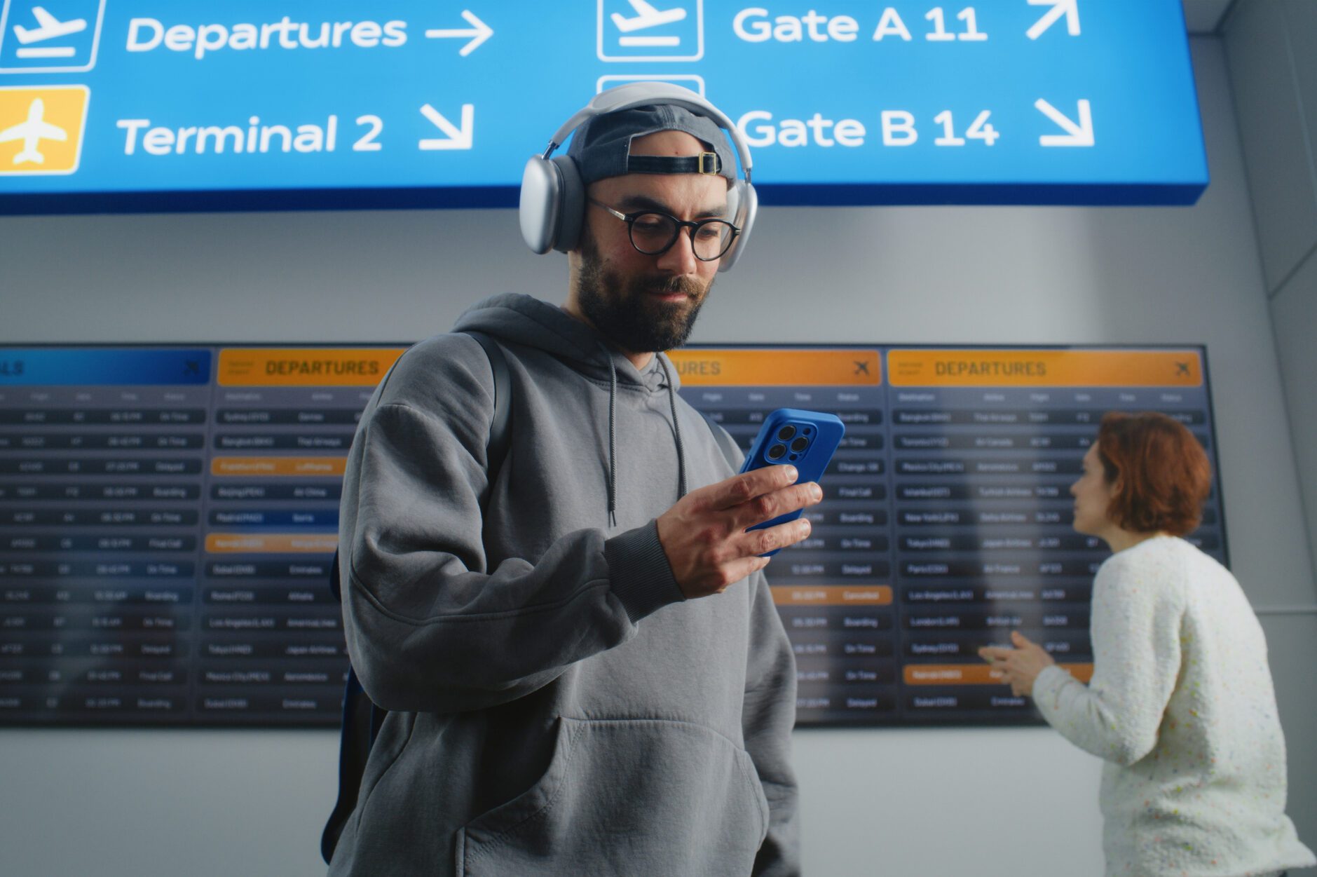 Man Checks Flight Information on Mobile Phone, Looks at Digital Arrival and Departure Board