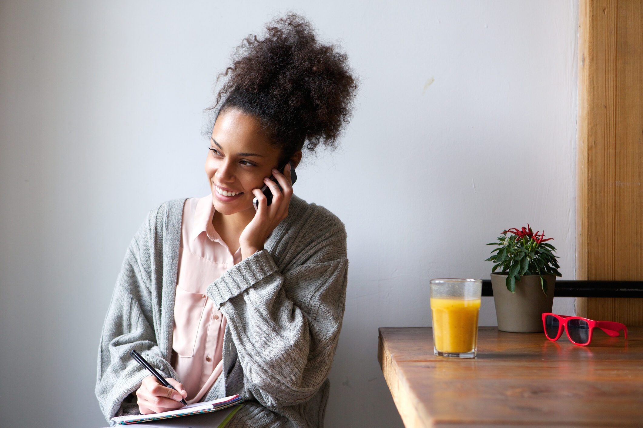 Young woman talking on mobile phone and taking notes