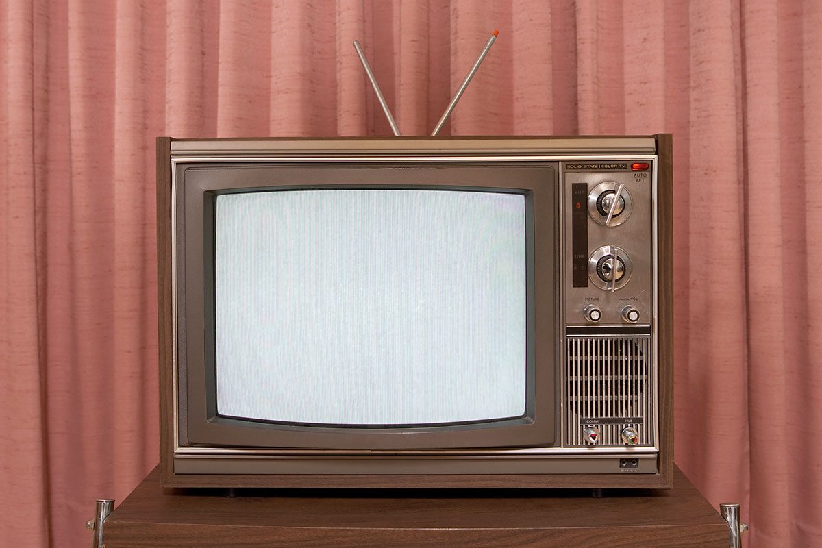 Old television on stand, in front of curtain