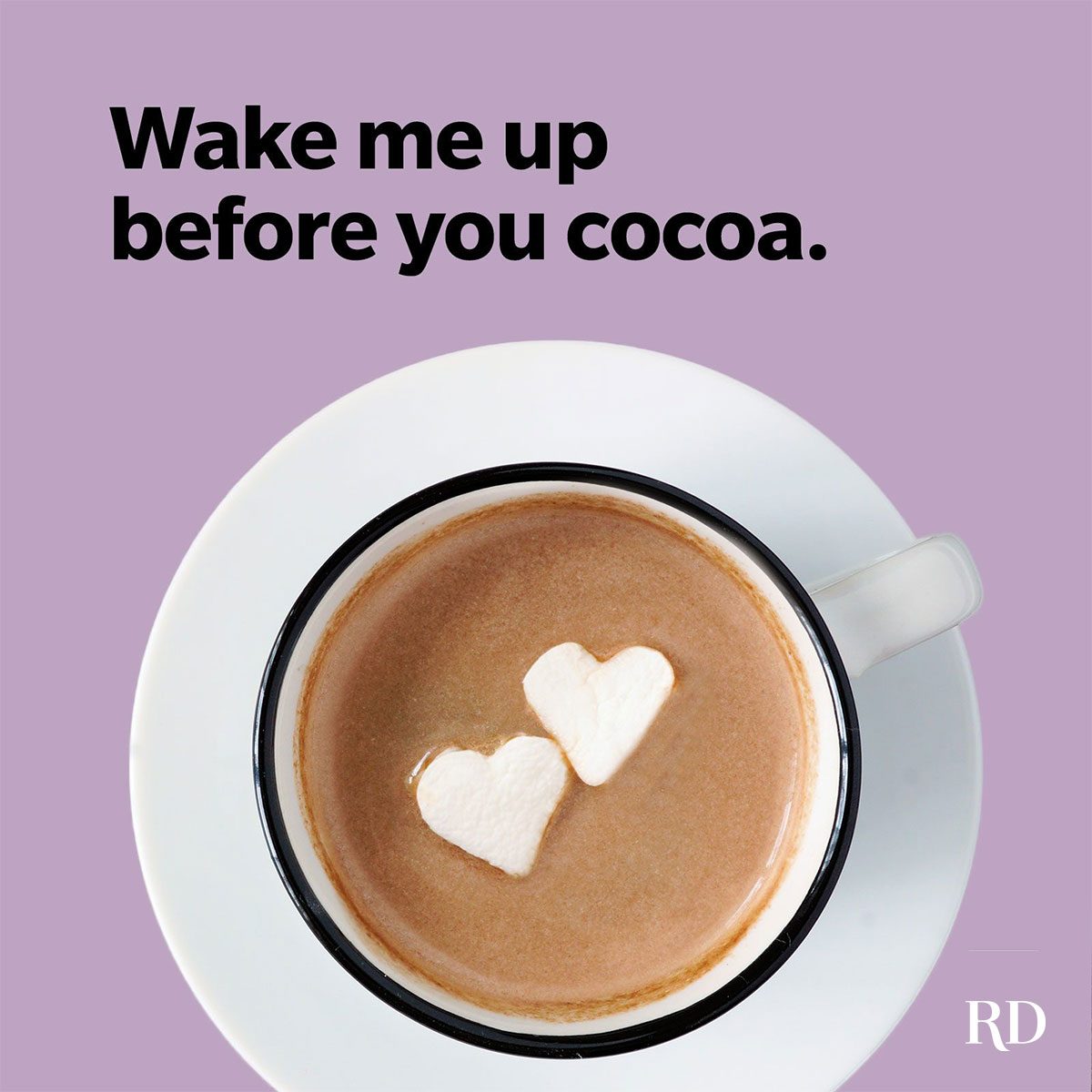 Cup contains hot cocoa with heart-shaped marshmallows. Text above reads, "Wake me up before you cocoa." Placed on a light purple background.