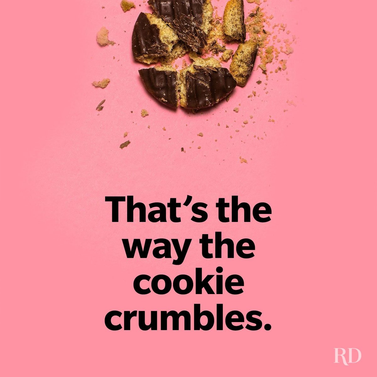 Broken chocolate cookie with scattered crumbs on a pink surface. Text reads: â€œThat's the way the cookie crumbles.â€
