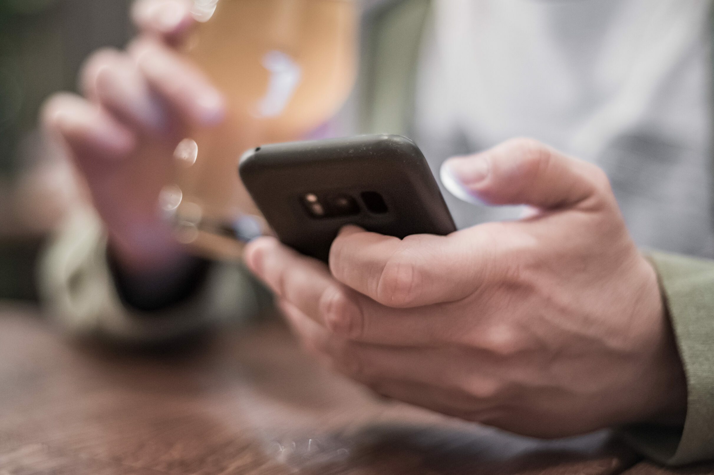 close up of man hand hold smartphone, drinking beer and reading message at bar or pub