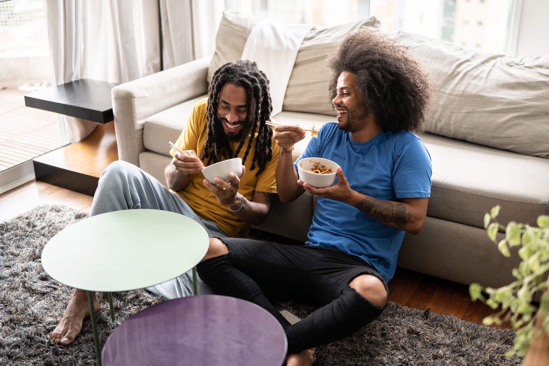Brothers sitting on the ground eating noodles at home