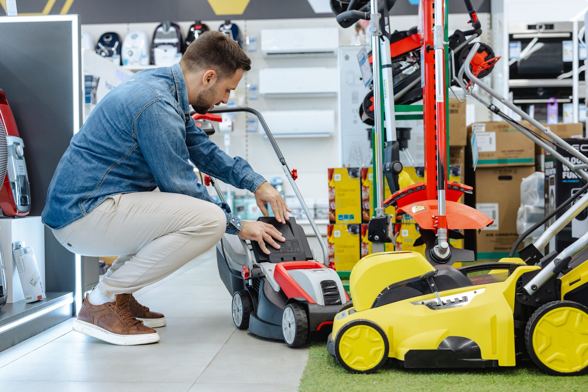 Man examining lawn mowers in a showroom for home gardening equipment
