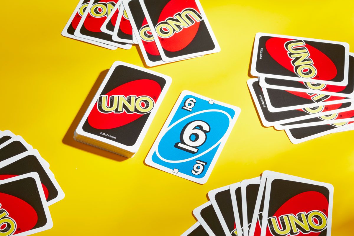 Beginning of an Uno game dealt out on yellow background; draw and discard piles in the center of four hands of cards dealt face down