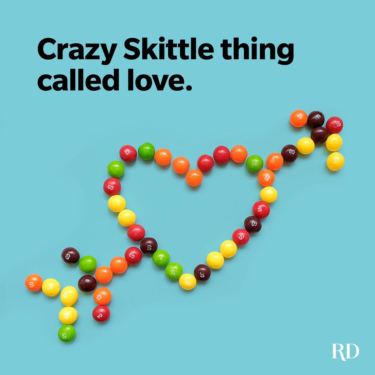 Skittles form a heart with an arrow on a blue background. Text reads, "Crazy Skittle thing called love."