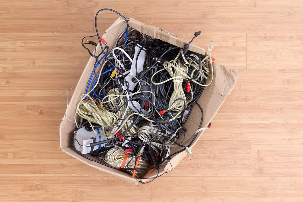 Old battered cardboard box with electrical cords and connectors for electronic devices on a wooden background